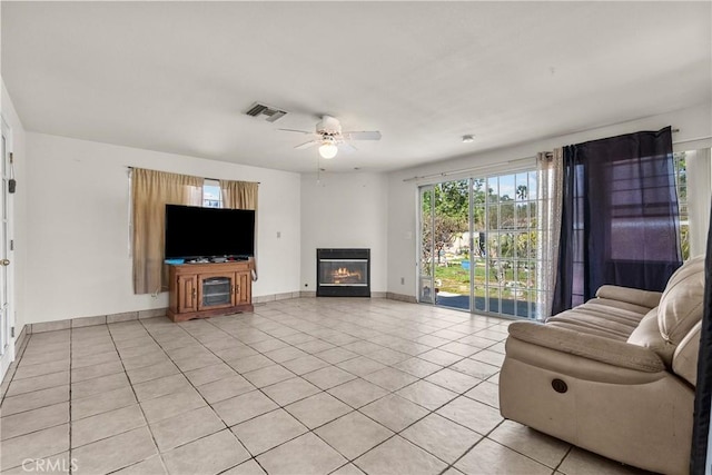 living room featuring visible vents, ceiling fan, baseboards, light tile patterned flooring, and a glass covered fireplace