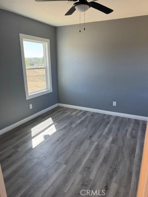 spare room with baseboards, dark wood finished floors, and a ceiling fan