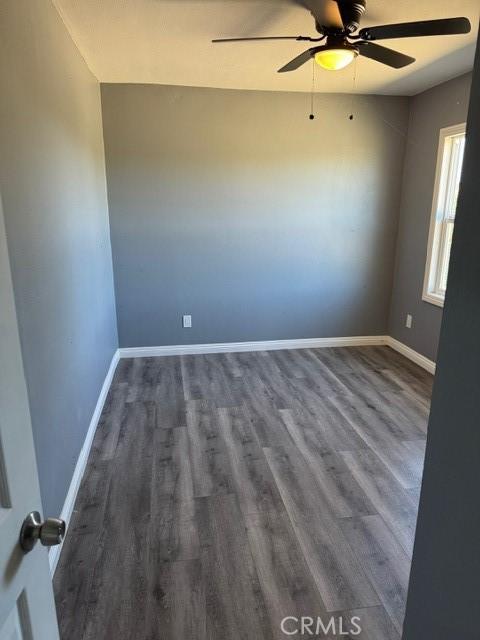 empty room featuring baseboards, a ceiling fan, and dark wood-style flooring