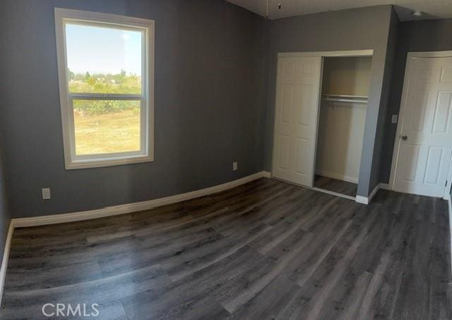 unfurnished bedroom featuring dark wood finished floors, a closet, and baseboards