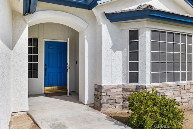 view of exterior entry featuring stone siding and stucco siding