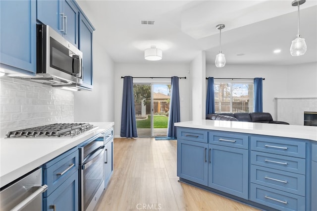 kitchen with blue cabinetry, backsplash, open floor plan, stainless steel appliances, and light countertops