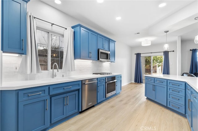 kitchen featuring light wood finished floors, tasteful backsplash, appliances with stainless steel finishes, blue cabinets, and a sink