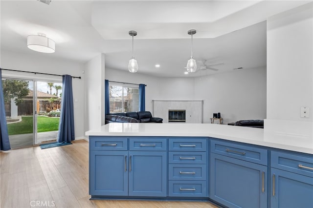 kitchen with a high end fireplace, light countertops, pendant lighting, blue cabinets, and light wood-type flooring