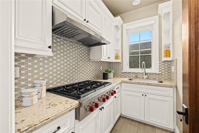 kitchen with a sink, under cabinet range hood, backsplash, white cabinetry, and stainless steel gas stovetop