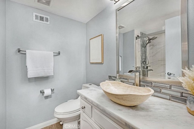 full bathroom with visible vents, toilet, tiled shower, and vanity