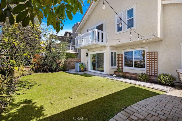 back of house with stucco siding, a balcony, central AC unit, and a lawn