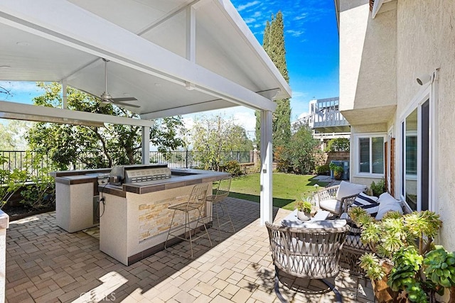 view of patio with ceiling fan, outdoor wet bar, an outdoor kitchen, and a fenced backyard