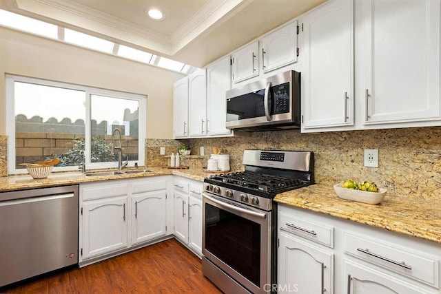 kitchen with ornamental molding, a sink, tasteful backsplash, appliances with stainless steel finishes, and white cabinets