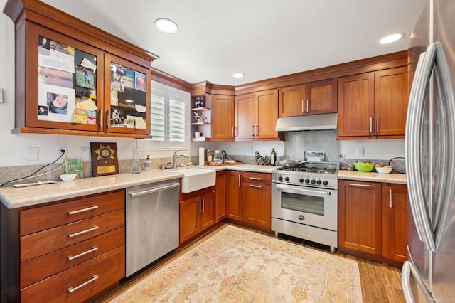 kitchen featuring under cabinet range hood, open shelves, a sink, appliances with stainless steel finishes, and brown cabinetry