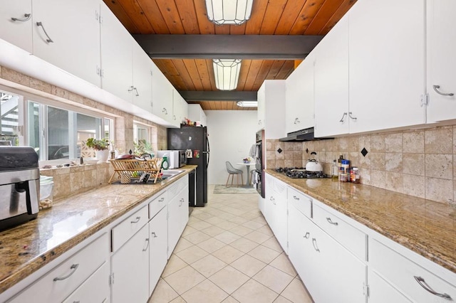 kitchen with beam ceiling, black appliances, under cabinet range hood, backsplash, and light tile patterned floors