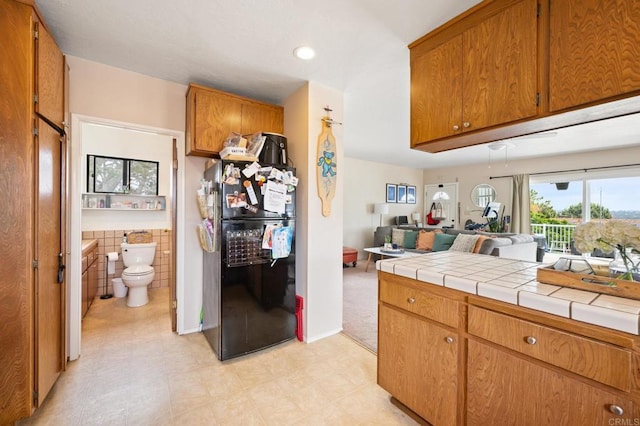 kitchen with open floor plan, light floors, brown cabinets, freestanding refrigerator, and tile walls