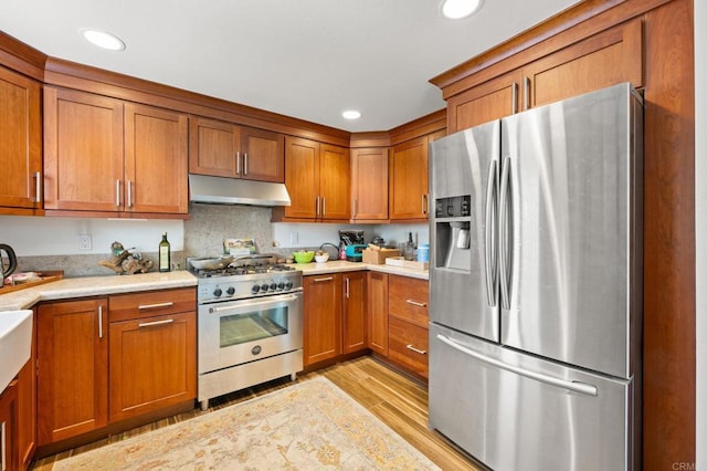 kitchen featuring light countertops, brown cabinetry, under cabinet range hood, and stainless steel appliances