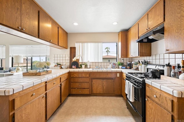 kitchen with black gas range oven, brown cabinetry, a wealth of natural light, and under cabinet range hood