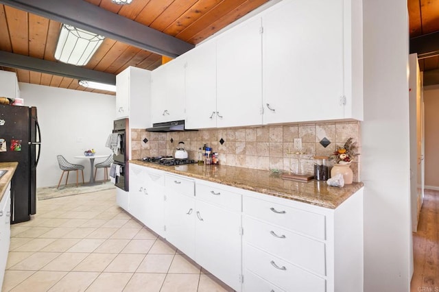 kitchen featuring under cabinet range hood, decorative backsplash, black appliances, and light tile patterned floors