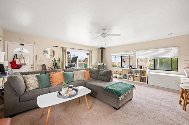 living room featuring carpet flooring, a healthy amount of sunlight, a wood stove, and a ceiling fan