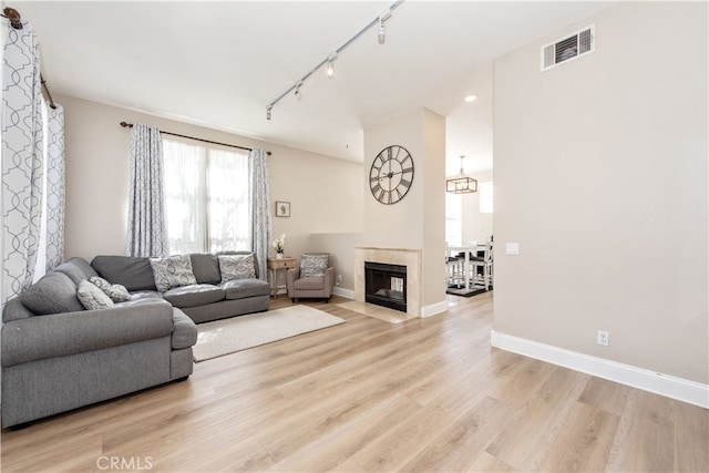 living area with visible vents, baseboards, a fireplace with flush hearth, track lighting, and light wood-style floors