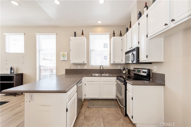 kitchen with dark countertops, appliances with stainless steel finishes, a peninsula, and white cabinets