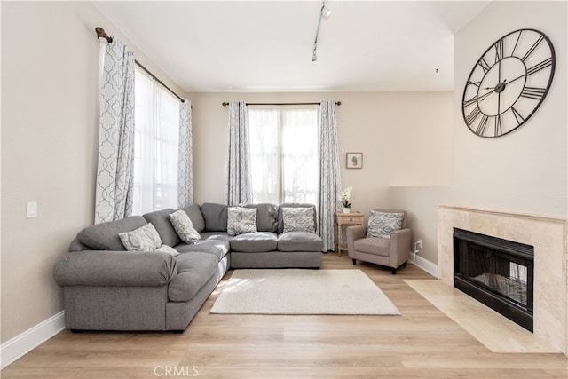 living room featuring rail lighting, wood finished floors, baseboards, and a high end fireplace