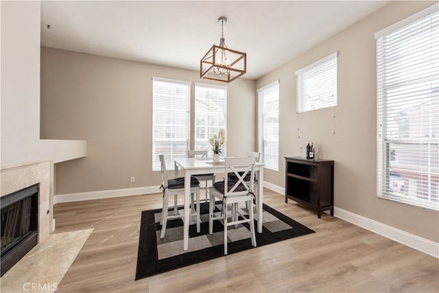 dining space featuring a notable chandelier, light wood-style flooring, a fireplace, and baseboards