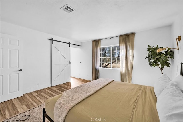 bedroom with a barn door, visible vents, and wood finished floors