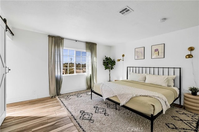 bedroom featuring a barn door, light wood-style floors, and visible vents