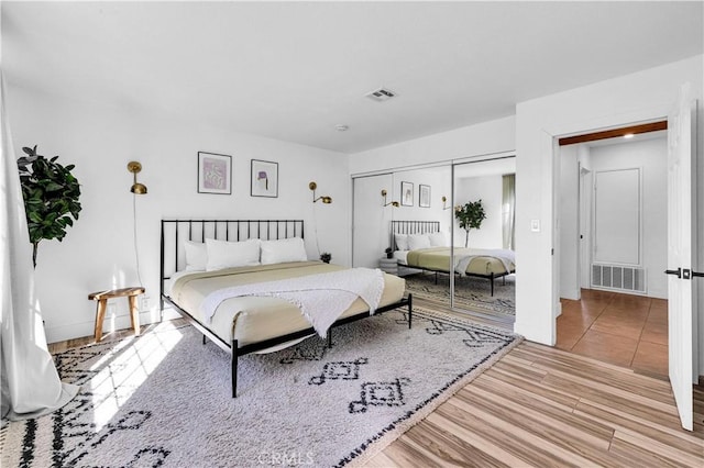 bedroom with wood finished floors, visible vents, and a closet