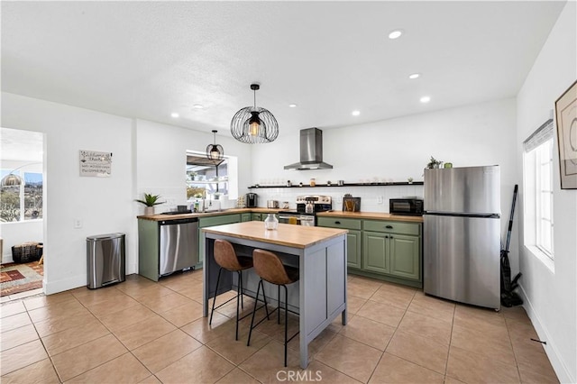 kitchen with wooden counters, light tile patterned flooring, stainless steel appliances, green cabinets, and wall chimney exhaust hood