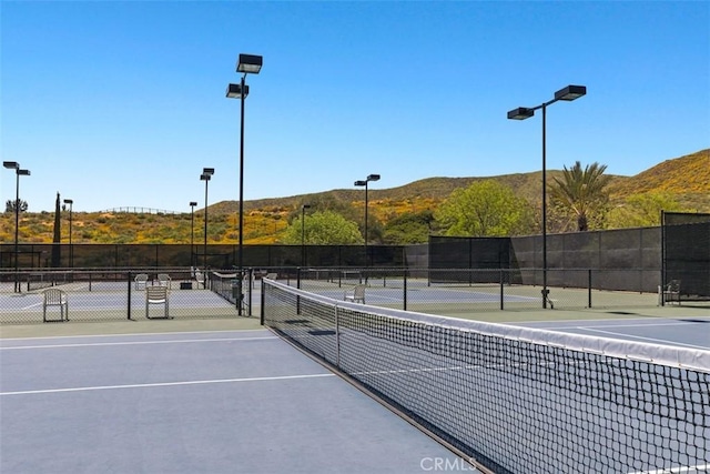 view of tennis court featuring a mountain view and fence