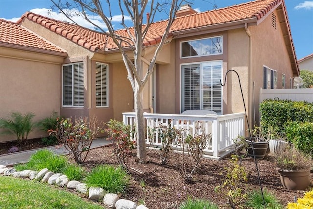 view of front of house featuring a tile roof, stucco siding, fence, and a chimney