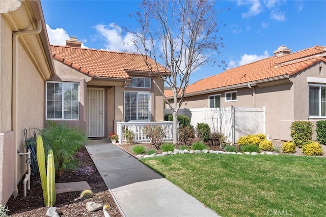 property entrance with stucco siding, a tiled roof, a chimney, and fence