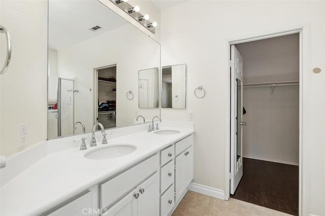 full bath featuring double vanity, visible vents, a walk in closet, and a sink