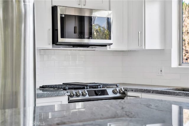 details with range, white cabinets, light stone counters, stainless steel microwave, and backsplash