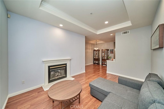 living area with light wood finished floors, visible vents, a raised ceiling, and a glass covered fireplace