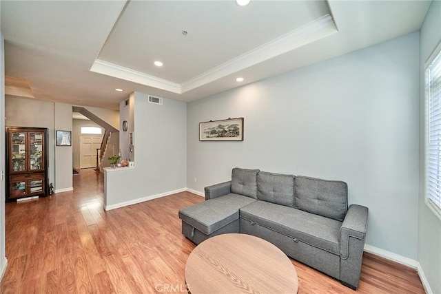 living room featuring light wood finished floors, visible vents, a raised ceiling, and stairway