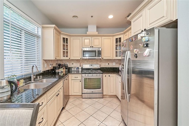 kitchen featuring light tile patterned flooring, a sink, stainless steel appliances, cream cabinets, and tasteful backsplash