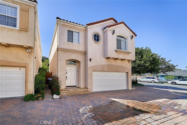 mediterranean / spanish home with stucco siding, a tile roof, decorative driveway, and a garage