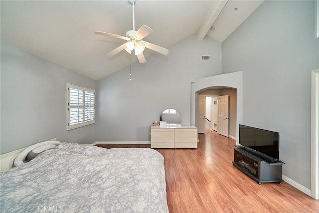 bedroom featuring baseboards, visible vents, light wood-style flooring, arched walkways, and beamed ceiling