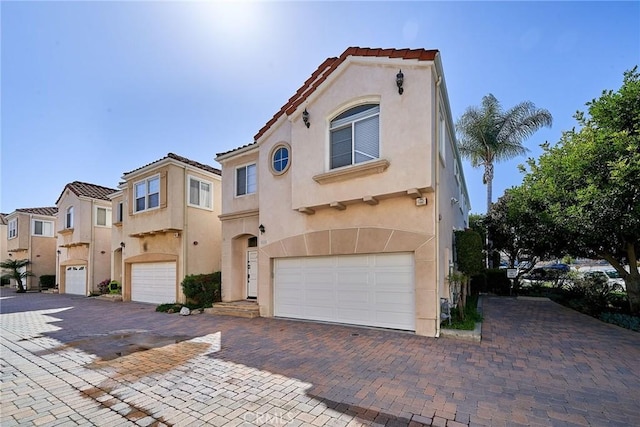 mediterranean / spanish-style home with stucco siding, decorative driveway, an attached garage, and a tile roof