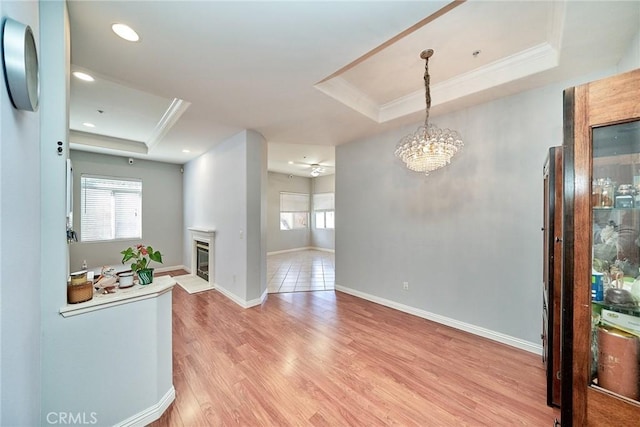 interior space featuring a glass covered fireplace, a tray ceiling, light wood-type flooring, and ornamental molding