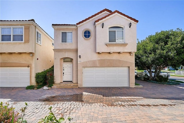 mediterranean / spanish-style home with stucco siding, a tiled roof, decorative driveway, and a garage