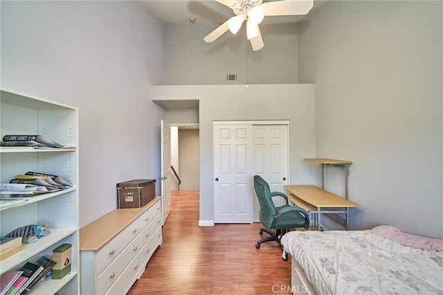 bedroom featuring visible vents, ceiling fan, a high ceiling, wood finished floors, and a closet