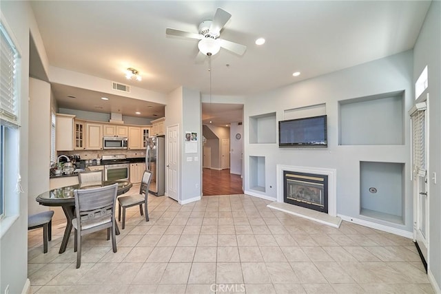 kitchen featuring visible vents, stainless steel appliances, cream cabinetry, a glass covered fireplace, and dark countertops