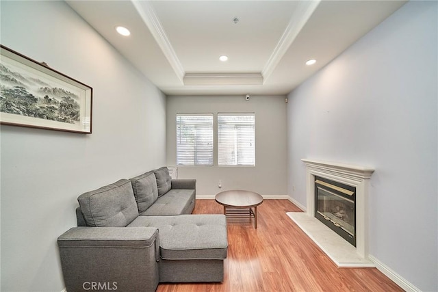 living area featuring light wood finished floors, baseboards, ornamental molding, a glass covered fireplace, and a raised ceiling