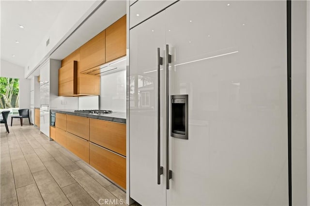 kitchen with paneled built in fridge, modern cabinets, light wood-type flooring, and stainless steel gas stovetop