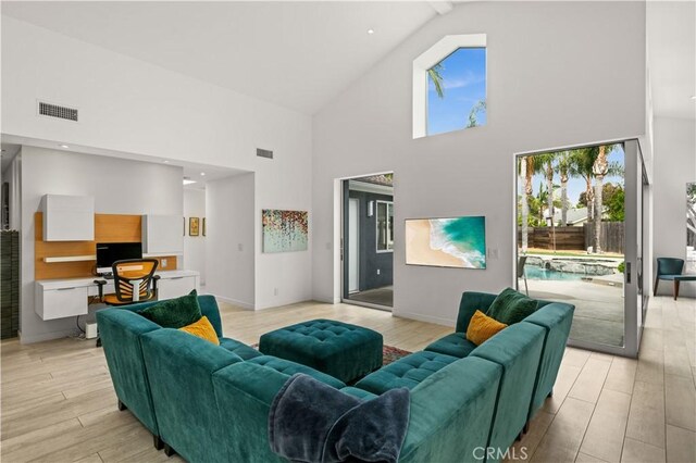 living area with high vaulted ceiling, visible vents, and light wood-type flooring