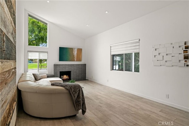 living area featuring a brick fireplace, wood finished floors, baseboards, and high vaulted ceiling