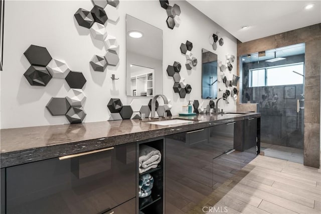 full bathroom featuring wood finished floors, tiled shower, double vanity, and a sink