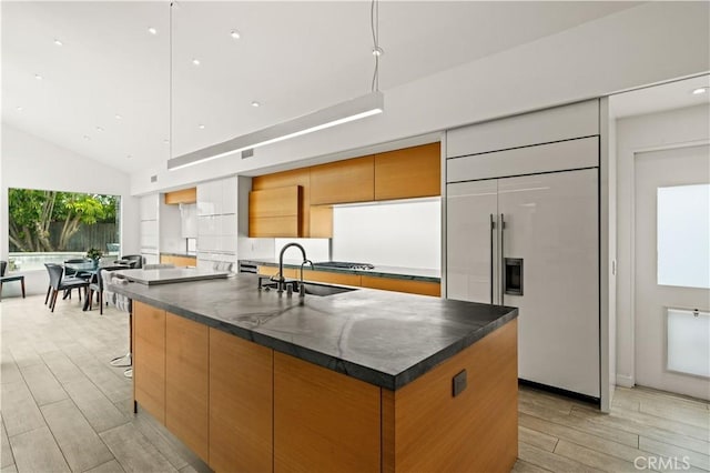 kitchen with a sink, paneled built in refrigerator, modern cabinets, and a kitchen island with sink