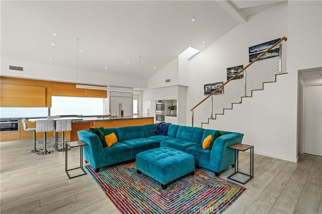 living area with stairway, visible vents, high vaulted ceiling, beamed ceiling, and light wood-type flooring